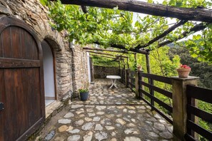 Ein von Pflastersteinen ausgelegter Außenbereich mit einer rustikalen Holzpergola, einem Tisch und Blumentöpfen.