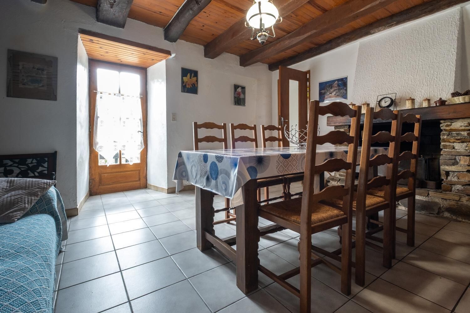 A dining area with a table set for four, wooden chairs, a chandelier, a fireplace, and a door leading outside.