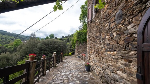 Um caminho de pedra leva a um edifício rústico com cerca de madeira e vasos com flores.