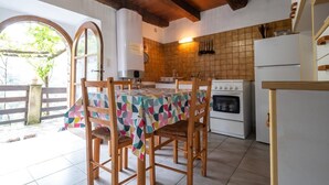 Uma cozinha com painel de azulejos, cadeiras de madeira, uma mesa com toalha colorida, fogão e geladeira.