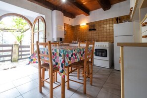 Eine Küche mit gefliestem Fliesenspiegel, Holzstühlen, einem Tisch mit bunten Tischdecken und einem Herd sowie einem Kühlschrank.