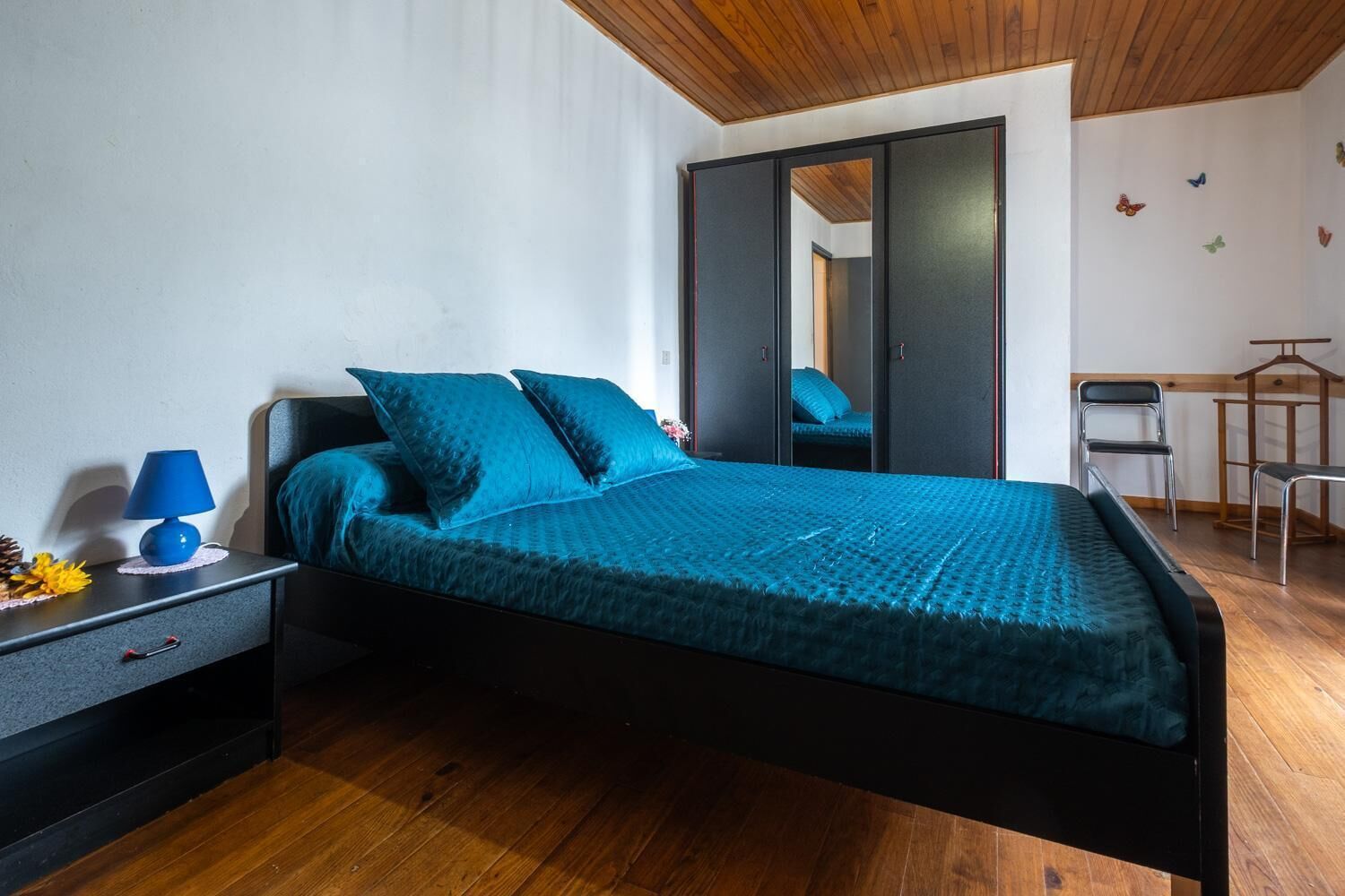Un dormitorio con cama, mesita de noche, lámpara, armario y silla.