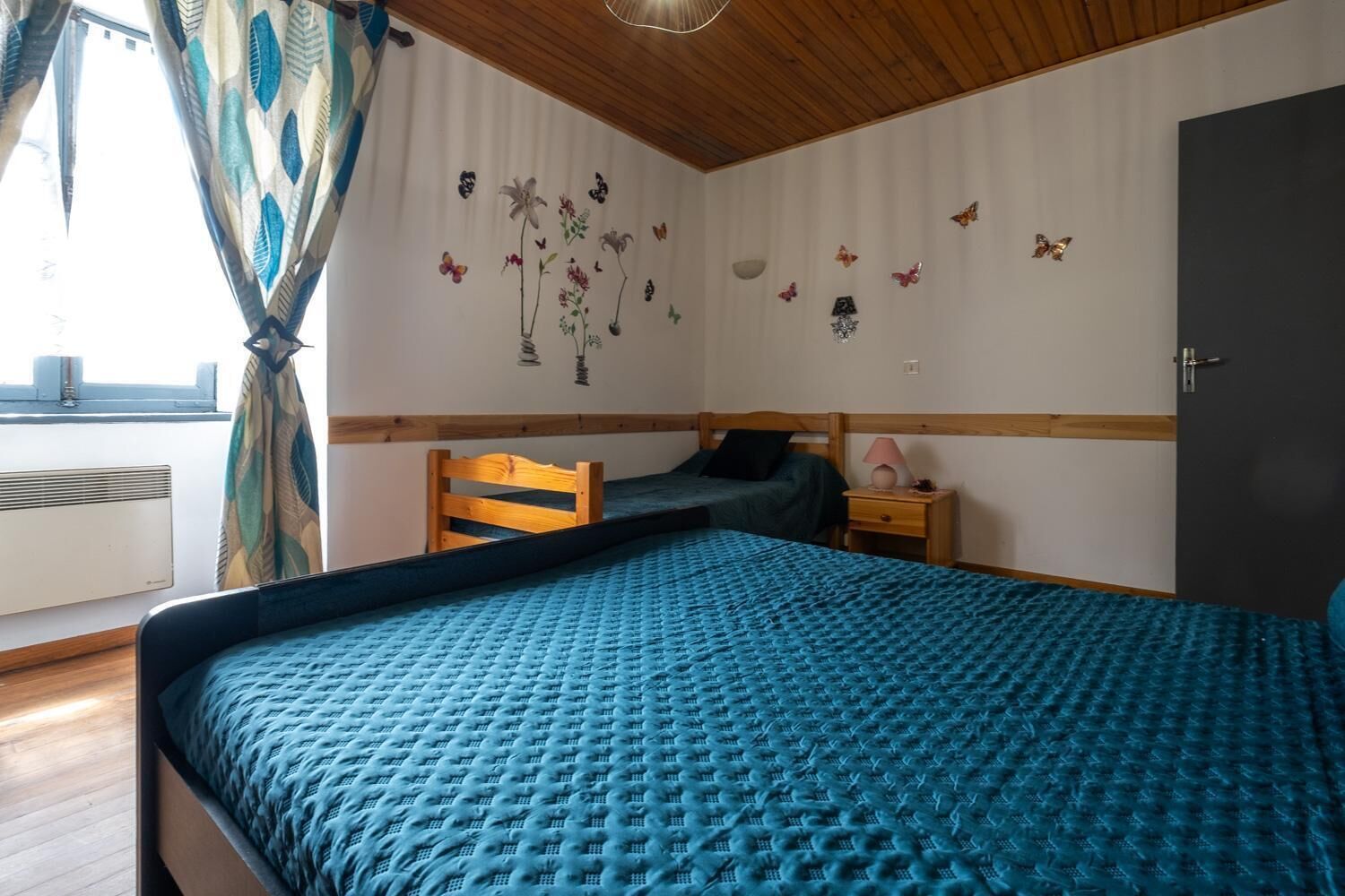 A bedroom with a bed, a smaller bed, a nightstand, a dresser, a window with curtains, and wall decorations.