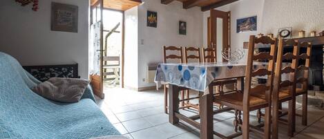 A room with a bed, a dining table with chairs, a hanging light fixture, and a fireplace.