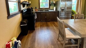 A compact kitchen with a dining area, wooden cabinets, a refrigerator, and a window.