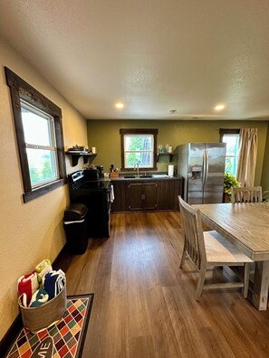 A compact kitchen with a dining area, wooden cabinets, a refrigerator, and a window. - Providence Rustic Retreat-Couples Getaway! (Woodburn)