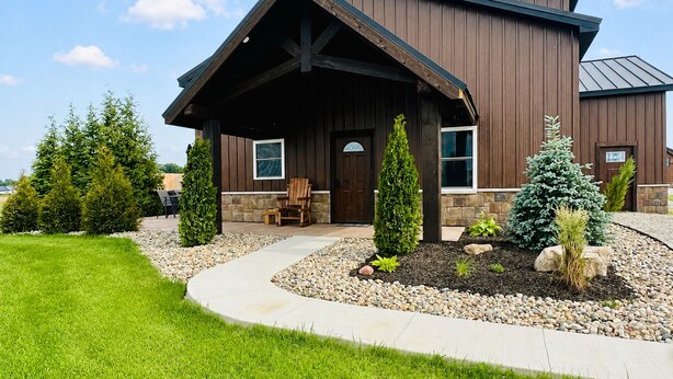 A modern two-story house with a covered porch, stone foundation, and a well-maintained lawn.