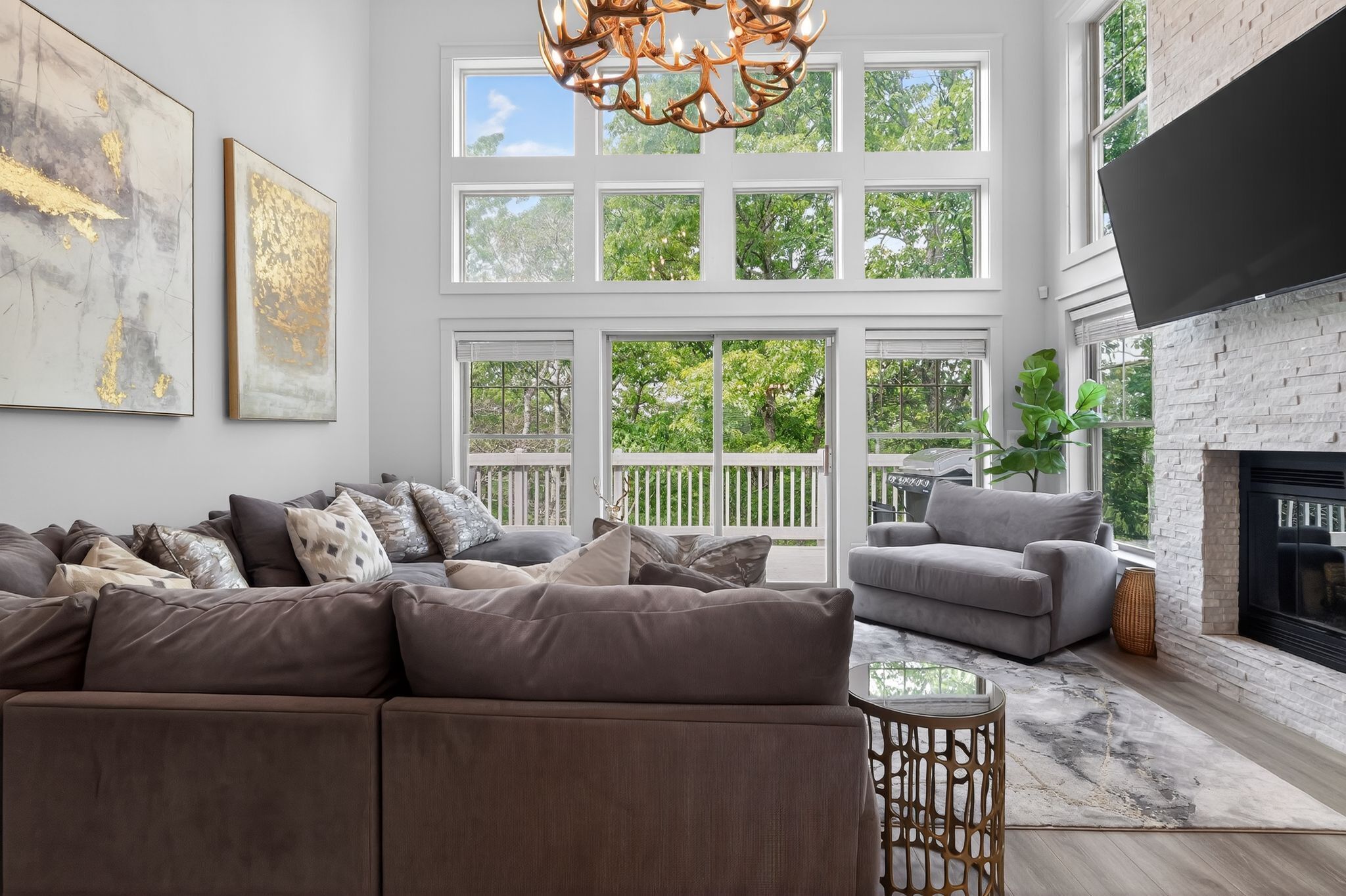 A spacious living room with a large sectional sofa, a smaller sofa, a fireplace, and large windows with a view of greenery.