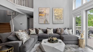 Ein modernes Wohnzimmer mit einem grauen Ecksofa, einem geometrischen Couchtisch und zwei abstrakten Bildern an der Wand.