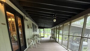 Ein überdachter Patio-Bereich mit Tisch und Stühlen, großen Fenstern und einem Deckenventilator.
