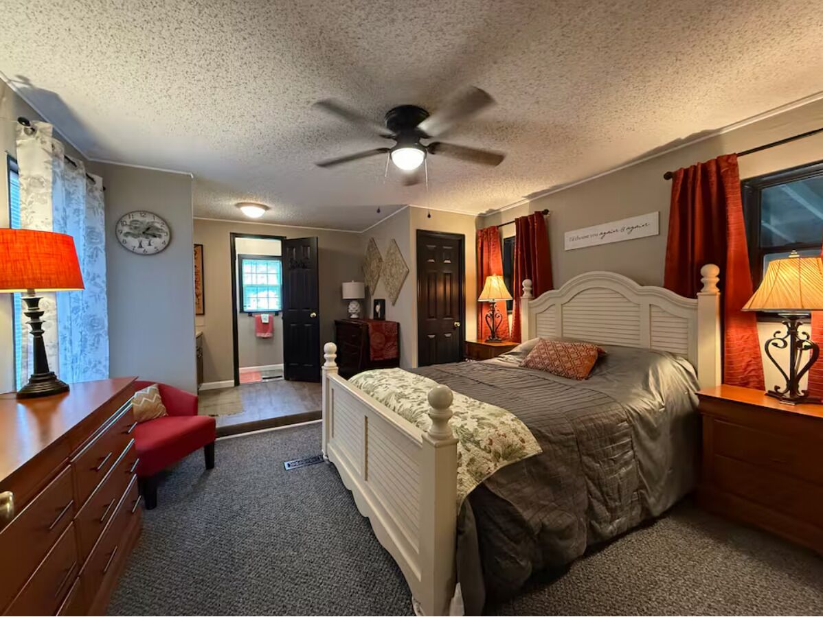 A bedroom with a bed, a desk, a chair, a ceiling fan, and a clock on the wall.