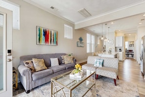 A spacious living room with a gray sofa, a patterned armchair, and a glass coffee table.