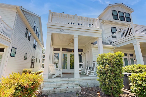 A two-story house with a porch, white railings, and a small tree in the foreground.