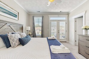 A bedroom with a bed, a nightstand, a dresser, a window with curtains, and a door.