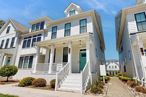 A row of two-story townhouses with a covered front porch, a green door, and a clear sky.