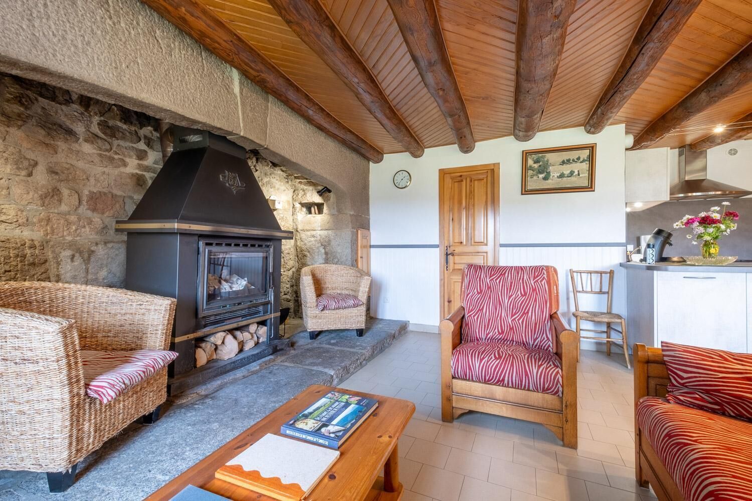 Ein gemütliches Wohnzimmer mit Steinwand, Kamin, Korbmöbeln und einer Küchenzeile.