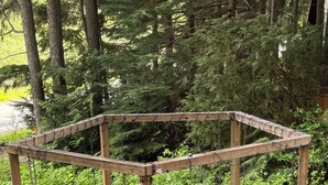 A wooden gazebo with benches, a fire pit, and a surrounding natural forest.