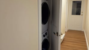 A laundry room with stacked washers and dryers, a wooden floor, and a white door with a glass panel.