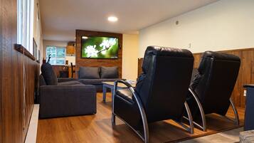 A modern living room with a sofa, two recliners, a coffee table, and a flat-screen TV mounted on a wooden wall.