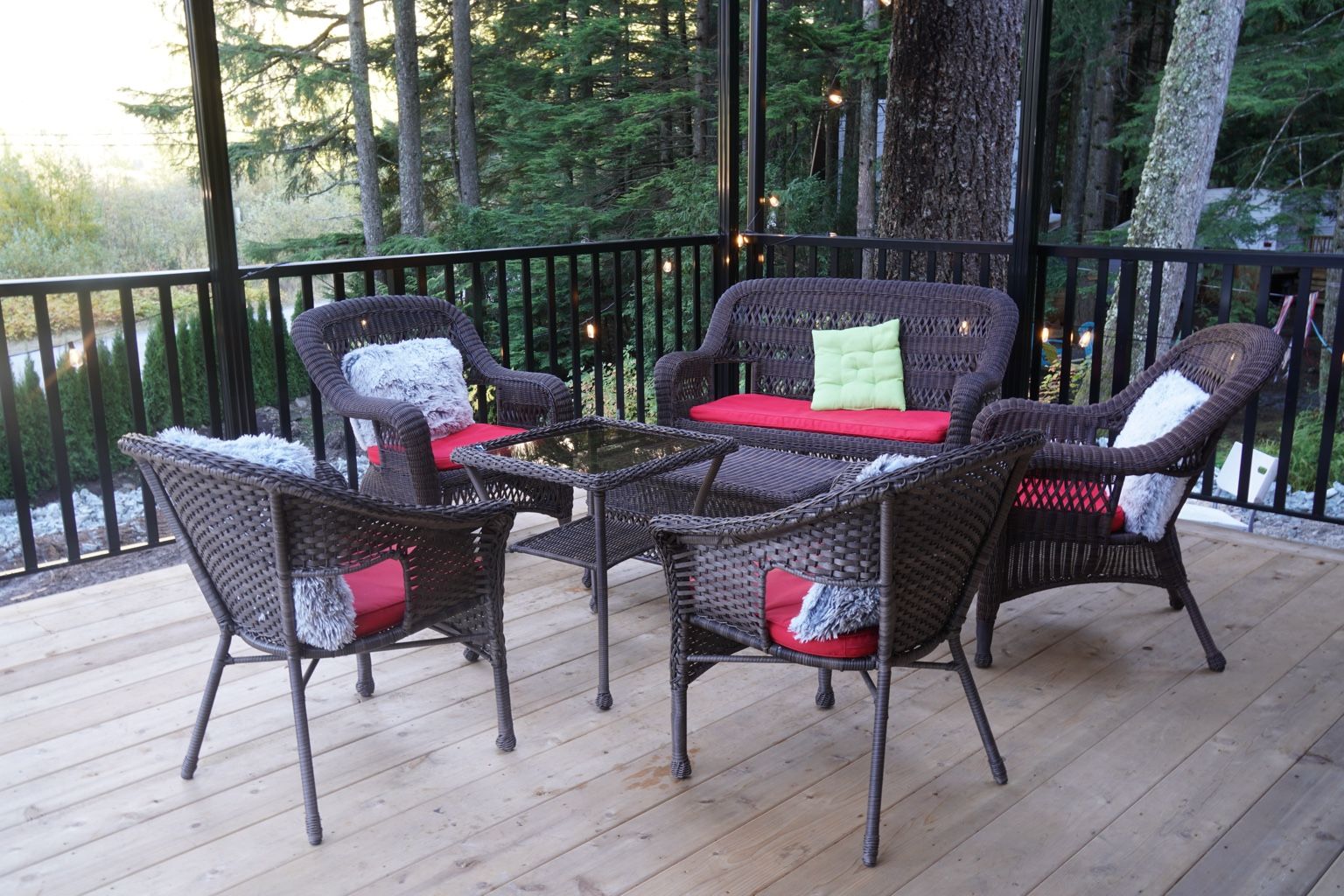 An outdoor deck with wicker furniture and a glass table.