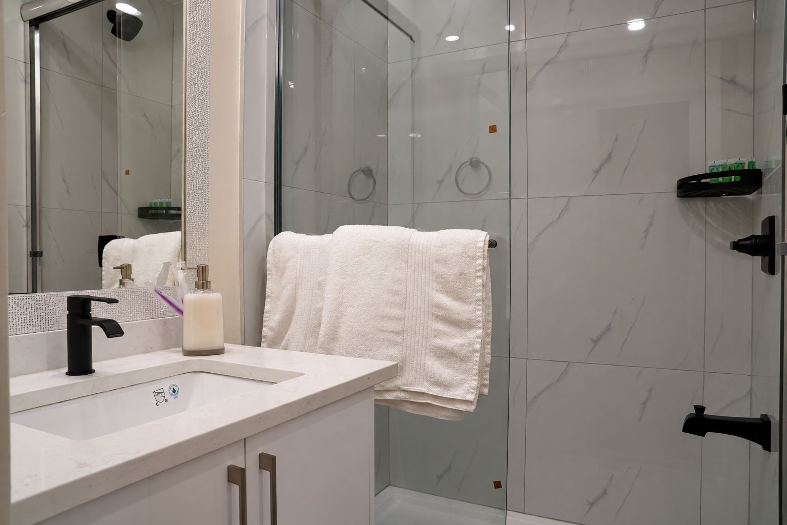 Un bagno con cabina doccia in vetro, lavandino bianco e specchio.