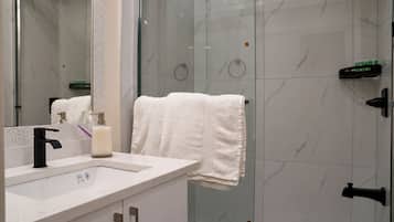 Un bagno con cabina doccia in vetro, lavandino bianco e specchio.