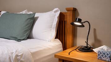 A neatly made bed with white and green pillows, a wooden headboard, a bedside table with a lamp, and a tissue box.