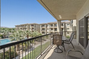 Un balcon donnant sur la piscine, un espace extérieur aménagé pour s’asseoir, et un immeuble avec de nombreux balcons en arrière-plan.