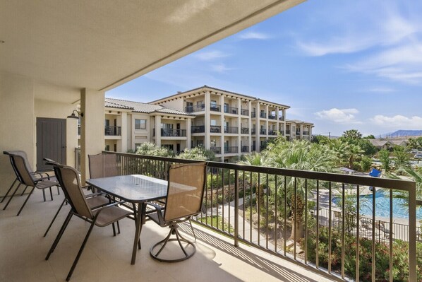 Un balcon avec une table et des chaises, donnant sur une piscine et un immeuble à plusieurs étages, lui aussi doté de balcons.