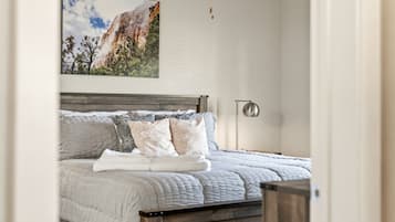 A bedroom with a bed, pillows, a blanket, a nightstand, a lamp, and a painting on the wall.