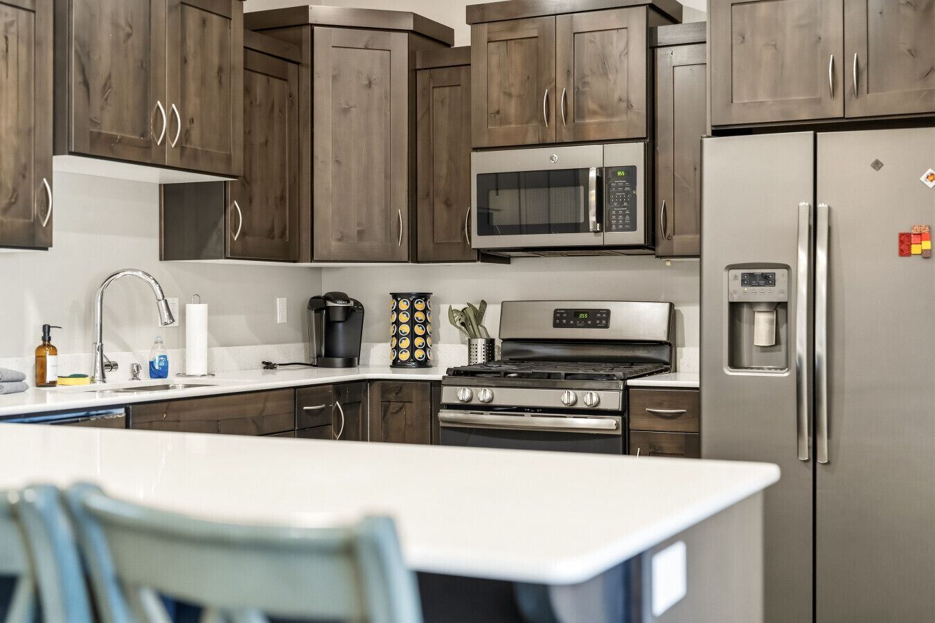 A modern kitchen with dark wooden cabinets, stainless steel appliances, a built-in microwave, and a refrigerator with a water dispenser.