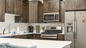 Eine moderne Küche mit dunklen Holzschränken, Edelstahlgeräten, einer eingebauten Mikrowelle und einem Kühlschrank mit Wasserspender.