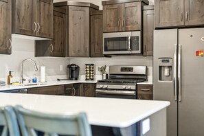 Eine moderne Küche mit dunklen Holzschränken, Edelstahlgeräten, einer eingebauten Mikrowelle und einem Kühlschrank mit Wasserspender.