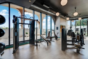 Un gimnasio con equipo de ejercicio, ventanas amplias y vista a la ciudad.