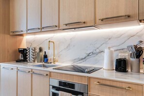 A modern kitchen with wooden cabinets, a marble countertop, a coffee maker, a toaster, and a paper towel holder. - Wynwood Pad- Stylish Apt with View & Rooftop Pool (Miami)