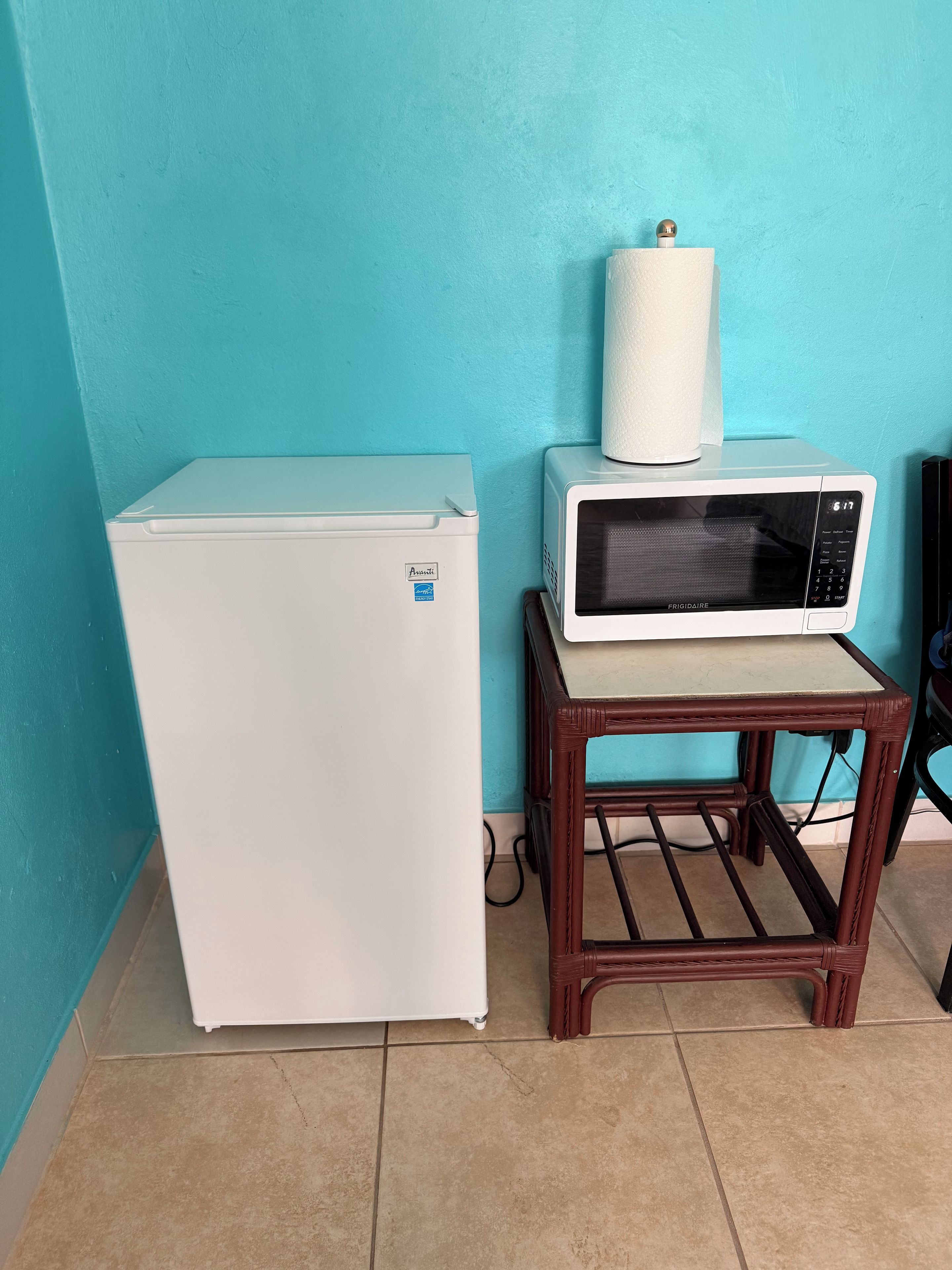 A compact kitchen area with a white refrigerator, a microwave on a wooden stand, and a blue wall.