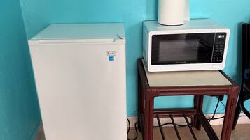 A compact kitchen area with a white refrigerator, a microwave on a wooden stand, and a blue wall.