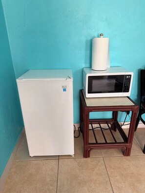 Un pequeño espacio de cocina con un refrigerador blanco, un microondas sobre un atril de madera y una pared azul.
