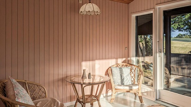 A room with a glass table, two wicker chairs, a door leading outside, and a hanging light fixture.