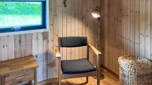 A room with wooden walls, a window with a view, a chair, a floor lamp, and a woven basket.