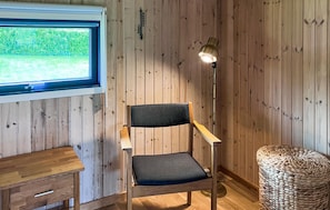 Ein Zimmer mit Holzwänden, einem Fenster mit Blick, einem Sessel, einer Stehlampe und einem gewebten Korb.