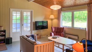 A cozy room with a sofa, a table, a chair, a TV, and large windows.