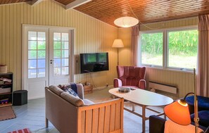 Ein gemütliches Zimmer mit einer Couch, einem Tisch, einem Stuhl, einem Fernseher und großen Fenstern.