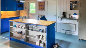A kitchen with blue cabinets, a wooden island with shelves, a coffee machine, and a hanging light fixture.