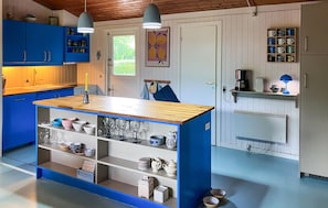 Eine Küche mit blauen Schränken, einer Holzeinzelinsel mit Regalen, einer Kaffeemaschine und einer Hängeleuchte.
