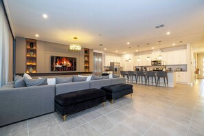 Ein modernes Wohnzimmer mit Ecksofa, Kamin und Küchenbereich mit Barhocker.