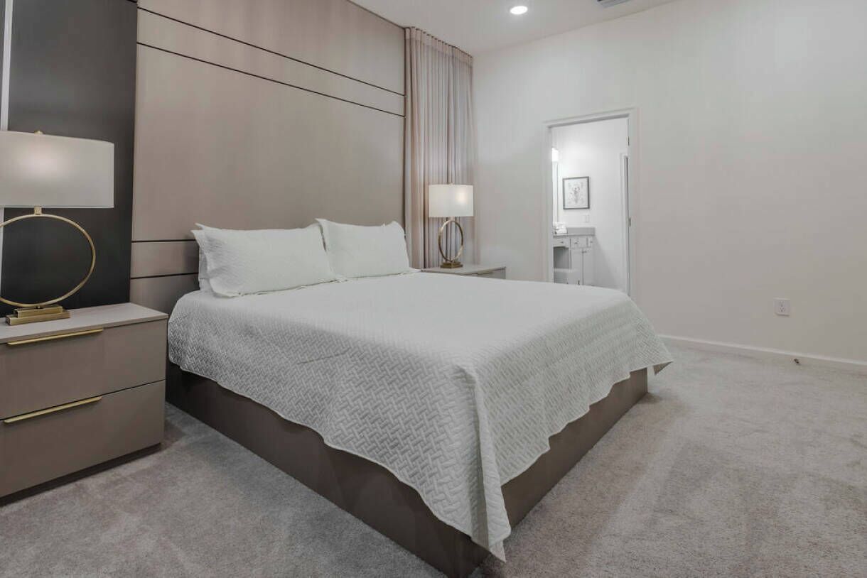 Un dormitorio moderno con una cama grande, mesitas de noche, una lámpara y un espejo.