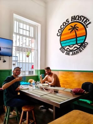 A dining area with a table, chairs, and a wall with a logo. - Cocos Hostel Rio (Rio de Janeiro)