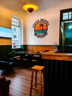 A cozy hostel interior with a wooden bar, seating area, and a wall-mounted TV. - Cocos Hostel Rio (Rio de Janeiro)