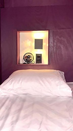 A bed with white linens, a window with a view, and a small table with a lamp and fan. - Cocos Hostel Rio (Rio de Janeiro)